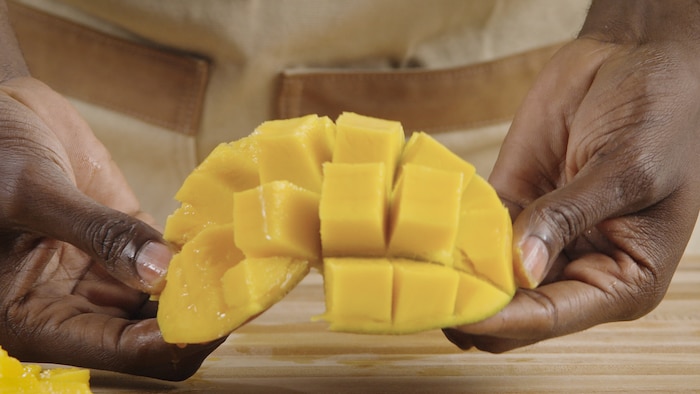 Une personne tient un morceau de mangue dans ses mains. 