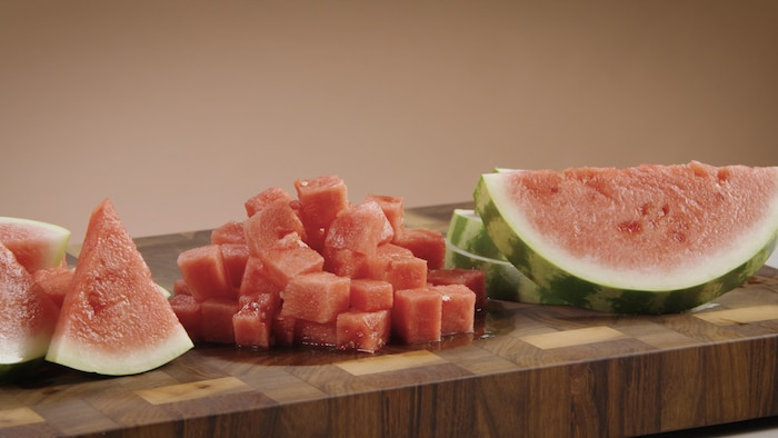 Un melon d'eau a été coupé en tranche et en cube. Les morceaux sont posés sur une table de travail. 