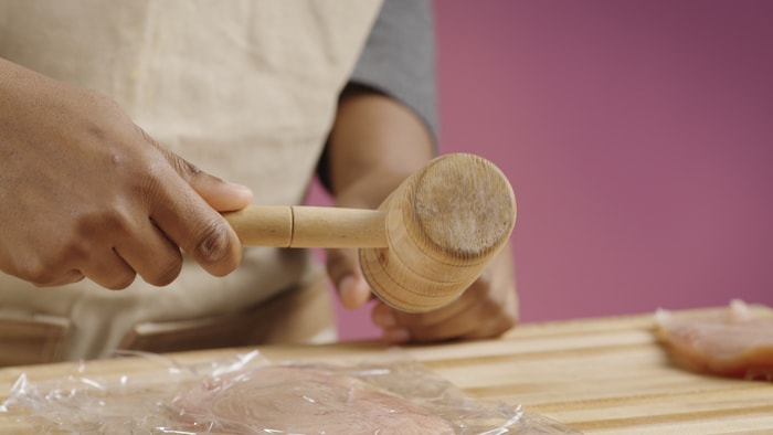 Une personne utilise son maillet attendrisseur sur le morceau de viande. 
 