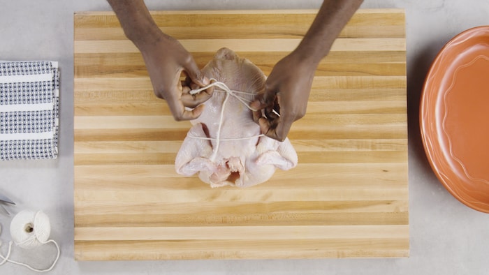 Une personne fait un nœud pour ficeler un poulet. 