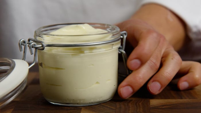Un petit pot transparent rempli de mayonnaise.