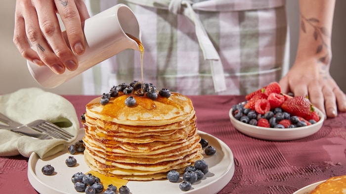 Une assiette avec une grosse pile de pancakes recouverts de bleuets et de sirop d'érable.