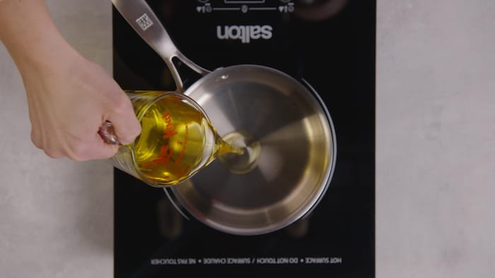 Une personne verse dans une casserole de l'huile de tournesol. 