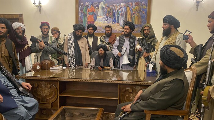 Des talibans assis autour d'un bureau de bois massif.