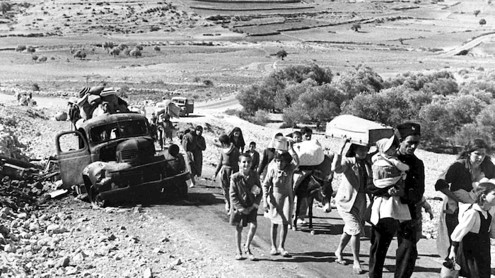 Une photo d'époque en noir et blanc avec des gens qui marchent en portant avec eux tous leurs biens dans un désert.