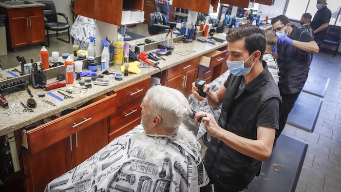 Des coiffeurs coiffent des clients avec un masque.