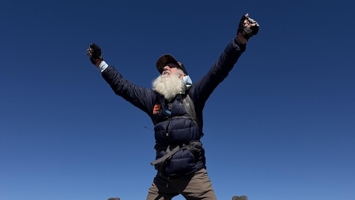 Dale Sanders célèbre son nouveau record en levant les bras en l'air, debout sur la pancarte en haut du sommet Katahdin, des Appalaches.