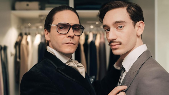Les deux hommes, vêtus de veston, regardent la caméra.