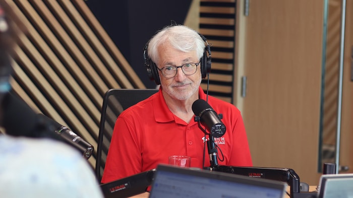 Il est assis devant un micro de radio.