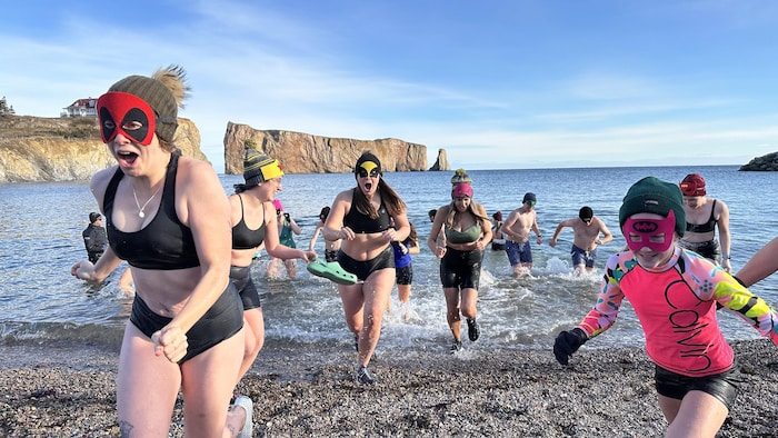 Un groupe de baigneurs sort de l'eau glacée avec le rocher Percé derrière eux.