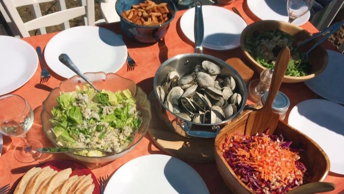 Une table remplie de plats contenant des salades et une marmite contenant des coques prêtes à manger.