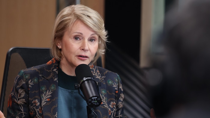 Geneviève Biron assise sur une chaise, parle dans un micro dans un studio de radio. 
