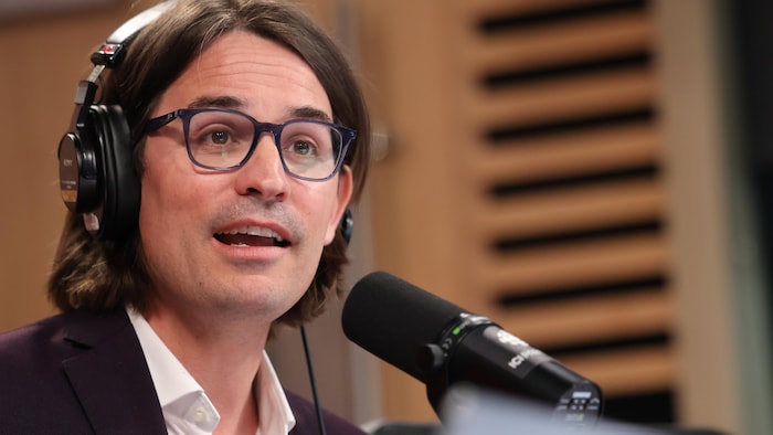 Jean-Denis Gagnon, casque d'écoute sur la tête, parle dans un micro, dans un studio de radio.