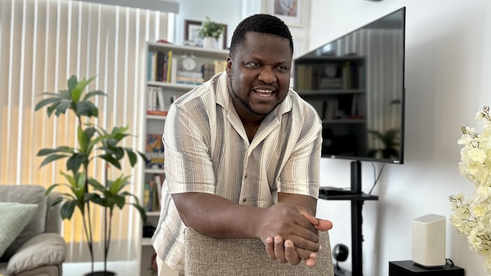 Thélyson Orélien, souriant, appuyé sur le dos d'une chaise.