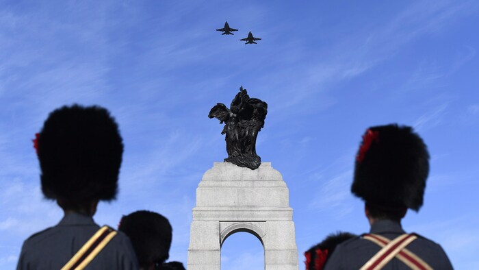 Des militaires en costume d'apparat observent le passage de deux avions CF-18 au-dessus du Monument commémoratif de guerre du Canada.