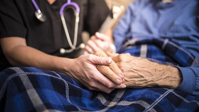 La main d'un soignant serrant la main d'une personne âgée.