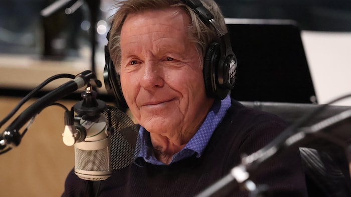 Rodger Brulotte parle dans un micro, dans un studio de Radio-Canada.