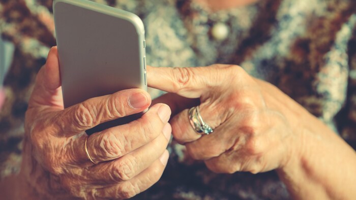 Les mains d'une femme âgée sur un téléphone cellulaire.