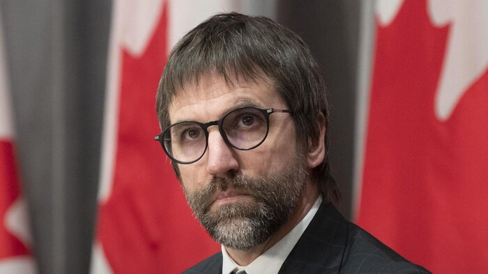 Steven Guilbault assis devant une rangée de drapeaux canadiens.
