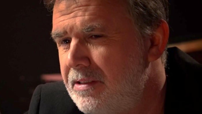 Un homme portant une barbe grise regarde devant lui.