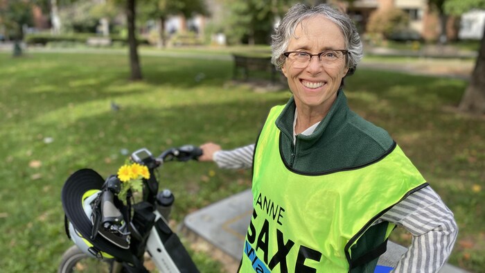 Habillée en gilet vert, Diane Saxe, debout dans un parc tient un vélo.