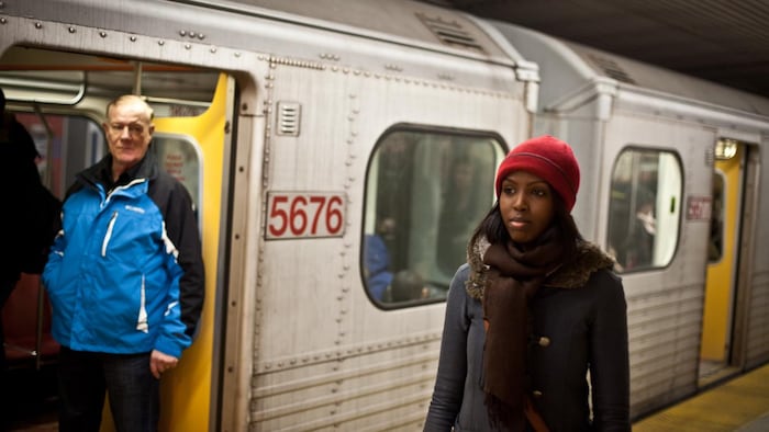 A woman in front of a subway train and a man looking at the camera.