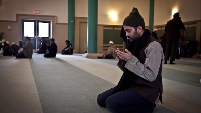 A man in his knees and hands in front of his chest, praying.