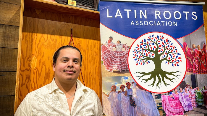 Un jeune homme à côté d'une bannière sur laquelle on peut lire "Latin Roots" (racines latines).