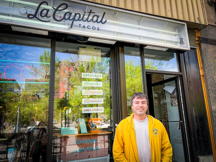 Un homme sourit à la caméra devant la façade de son restaurant.