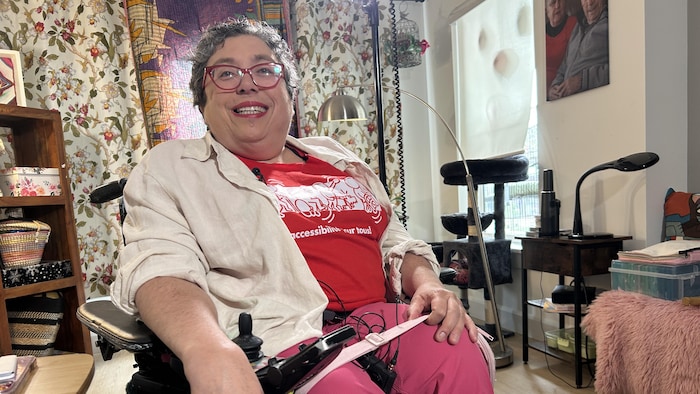 Murielle Pitre, dans son salon, porte un t-shirt sur lequel il est écrit «accessibilité pour tous».