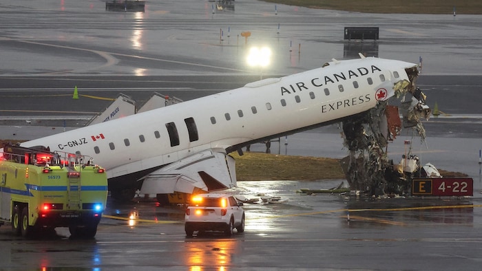 Sur une piste d'atterrissage, un avion dont le nez est relevé et dont le fuselage est éventré, entouré de véhicules d'urgence.