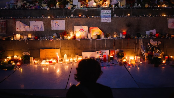 Des bougies illuminent des messages et des fleurs déposées dans un escalier.