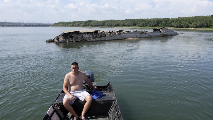 Un pêcheur dans sa chaloupe s'éloigne d'une épave sur un fleuve.
