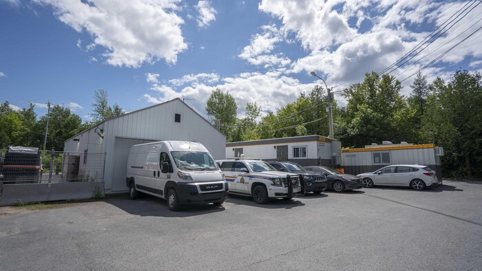 Des véhicules de la Gendarmerie royale du Canada sont garés devant un hangar et des roulottes de chantier.