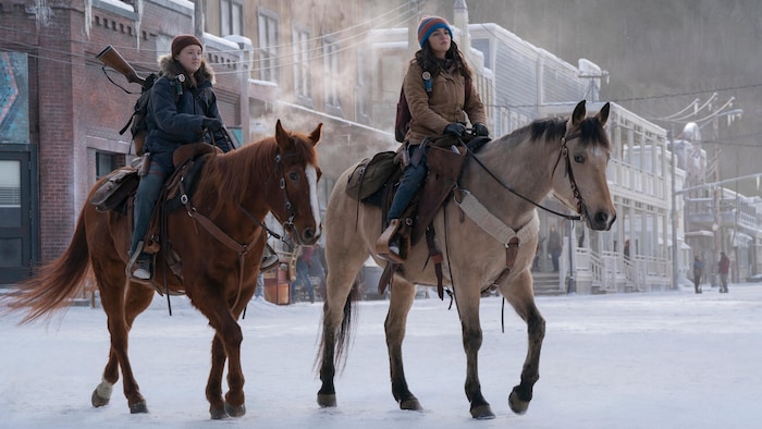 Deux acteurs avancent à cheval dans une rue.