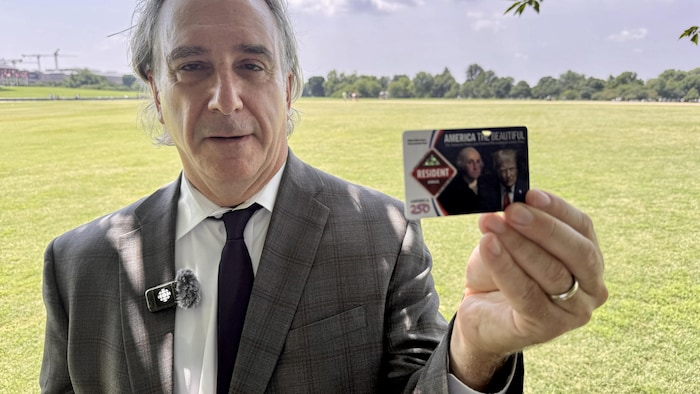Edward Lengel, ancien historien en chef de l'Association historique de la Maison-Blanche debout dans un parc. Il tient à la main un laissez-passer pour les parcs nationaux américains sur lequel on retrouve le visage de Georges Washington et celui de Donald Trump.