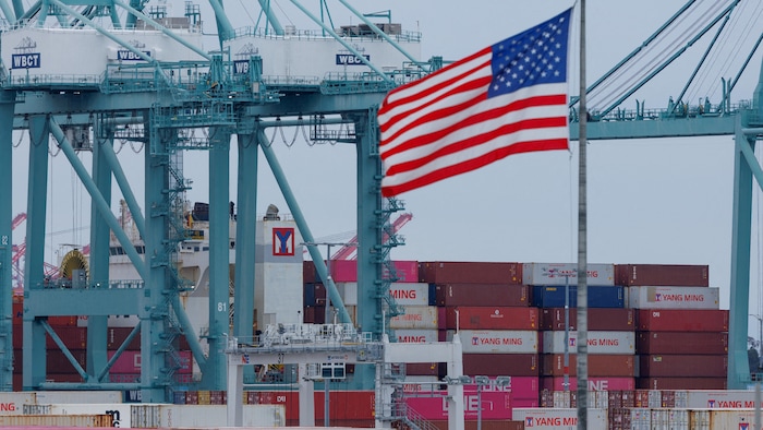 Un drapeau américain devant des conteneurs dans un port.