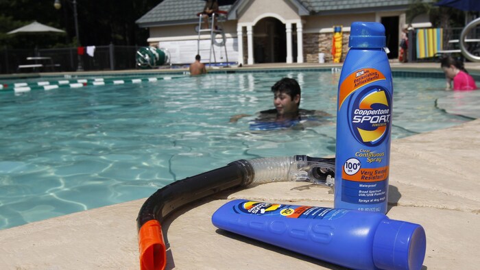 Deux flacons de lotion solaire sur le bord d'une piscine où un enfant se baigne. 