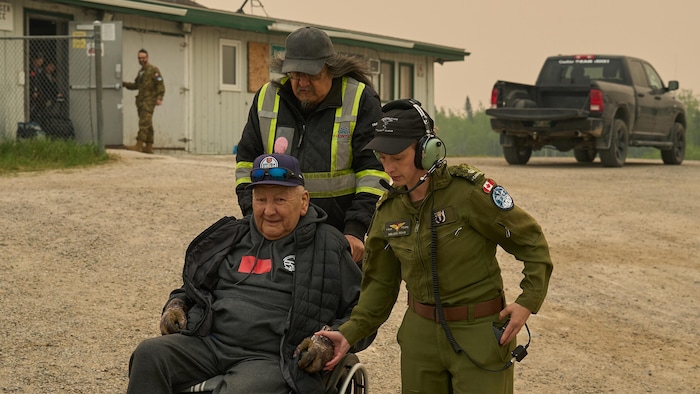 Un homme et une femme qui porte des habits militaires aident un homme âgé en fauteuil roulant.