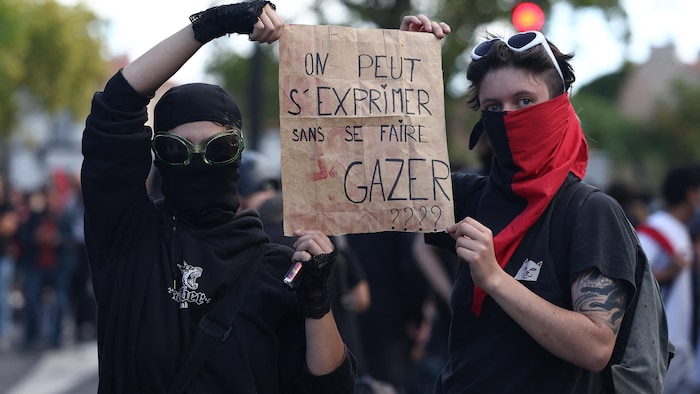Deux étudiants masqués brandissent un écriteau sur lequel on peut lire: «On peut s'exprimer sans se faire gazer????».