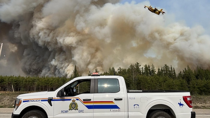 Une camionnette de la GRC et un avion-citerne près d'un feu de forêt.