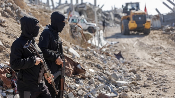 Des militants armés et cagoulés du Hamas devant des gravats à Gaza.