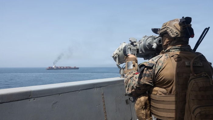 Un militaire observe un navire au loin avec un instrument d'optique.