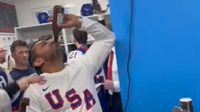 Un homme portant un gilet avec l'inscription « USA » boit une bière dans le vestiaire de l'équipe américaine de hockey.