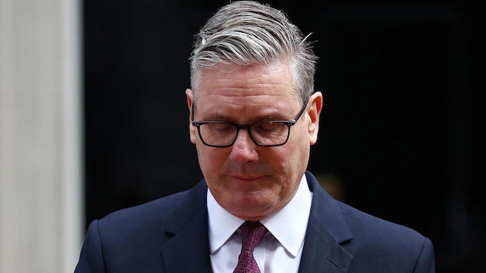 Le premier ministre britannique Keir Starmer derrière un lutrin, devant le 10 Downing Street, regarde vers le bas.