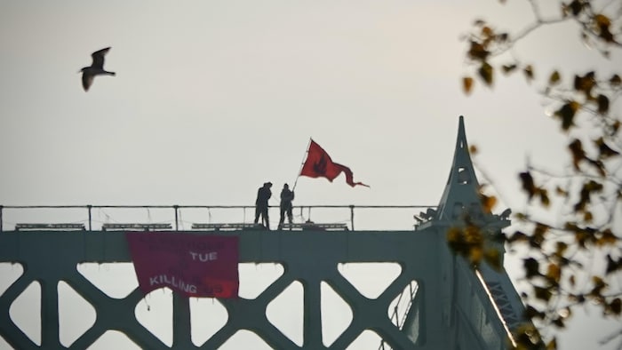 Deux personnes brandissent un drapeau au sommet d'un pont.