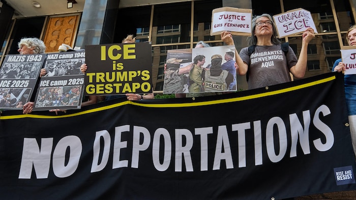 Des manifestants se tiennent derrière une grande banderole avec le message « No deportations » (pas d'expulsions, en français) et brandissent des pancartes.
