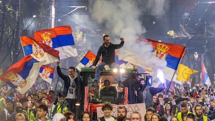 Une manifestation en Serbie. Certains manifestants brandissent des drapeaux serbes, tandis que d'autres sont assis sur un tracteur et lèvent le poing.