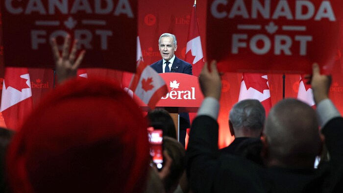 Mark Carney livre un discours à un podium devant des militants du Parti libéral du Canada qui tiennent des affiches.
