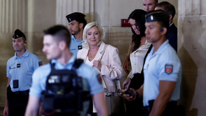 Marine Le Pen, entourée de gendarmes, sort d'un palais de justice.